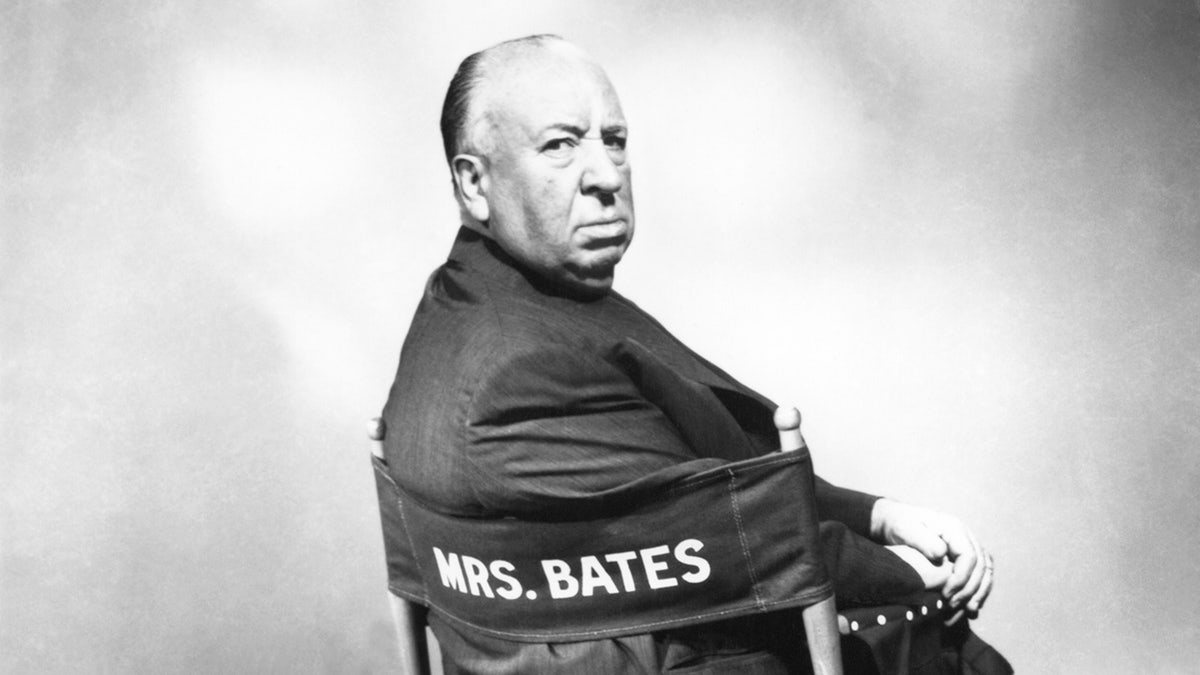 Alfred Hitchcock looking from behind his back while sitting on a directors chair