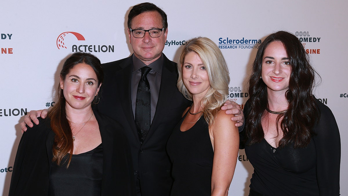 Bob Saget wearing a suit with his two daughters and wife Kelly Rizzo as they wear matching black outfits