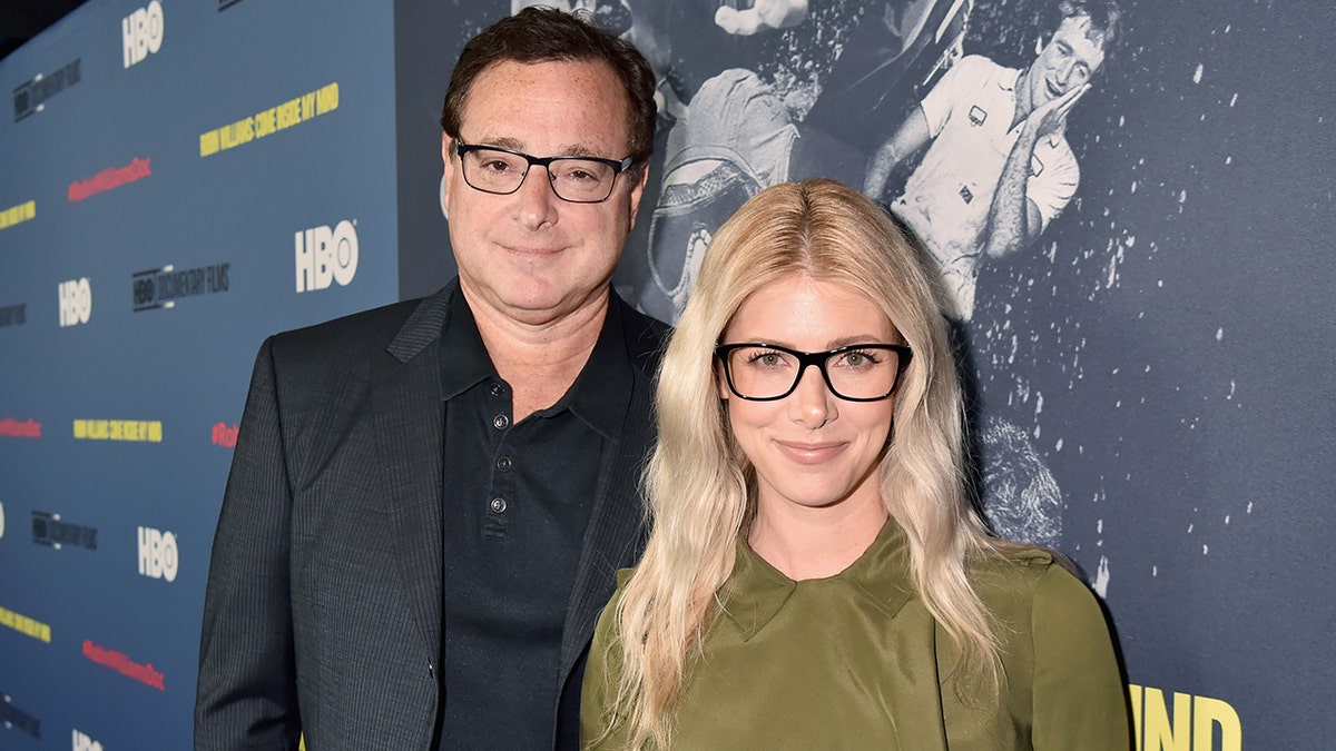 Bob Saget and Kelly Rizzo wearing matching glasses looking directly up front and smiling