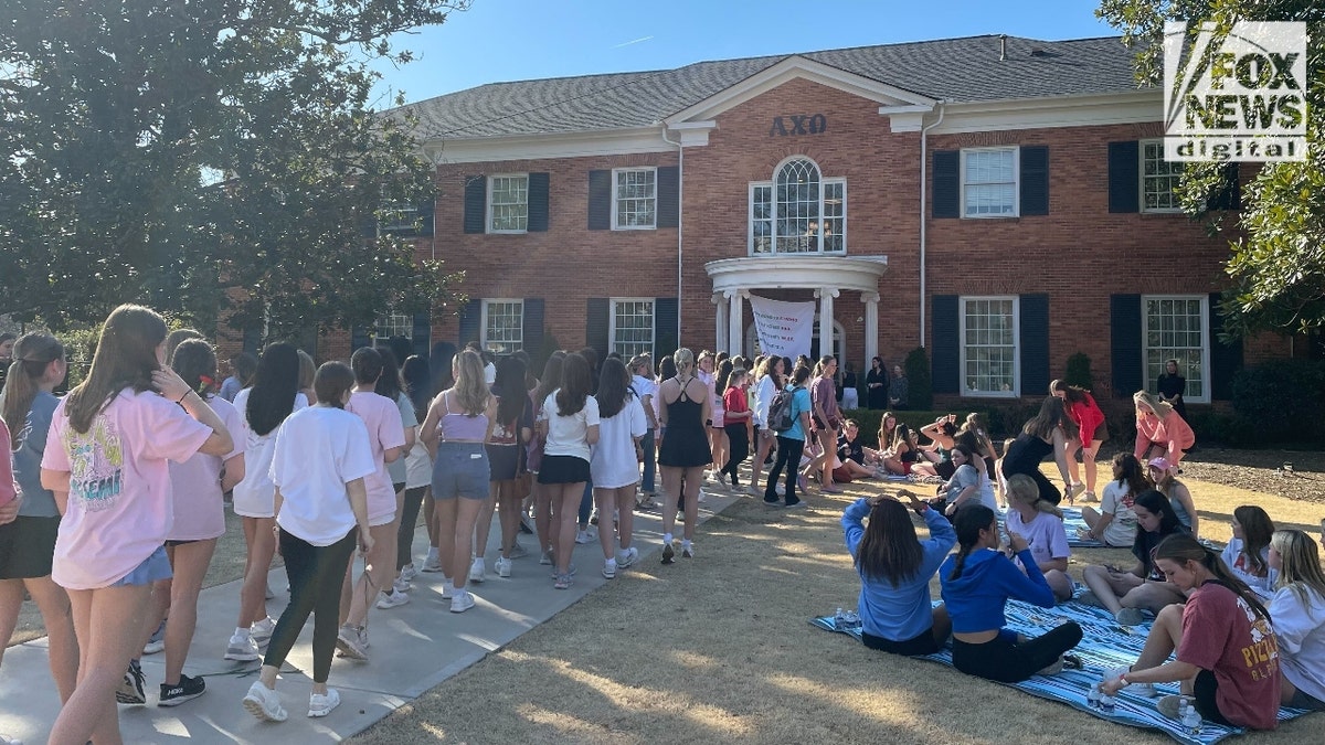 Dozens of female UGA students walking in a single-file line to place roses at the Alpha Chi Omega house on the school's campus.