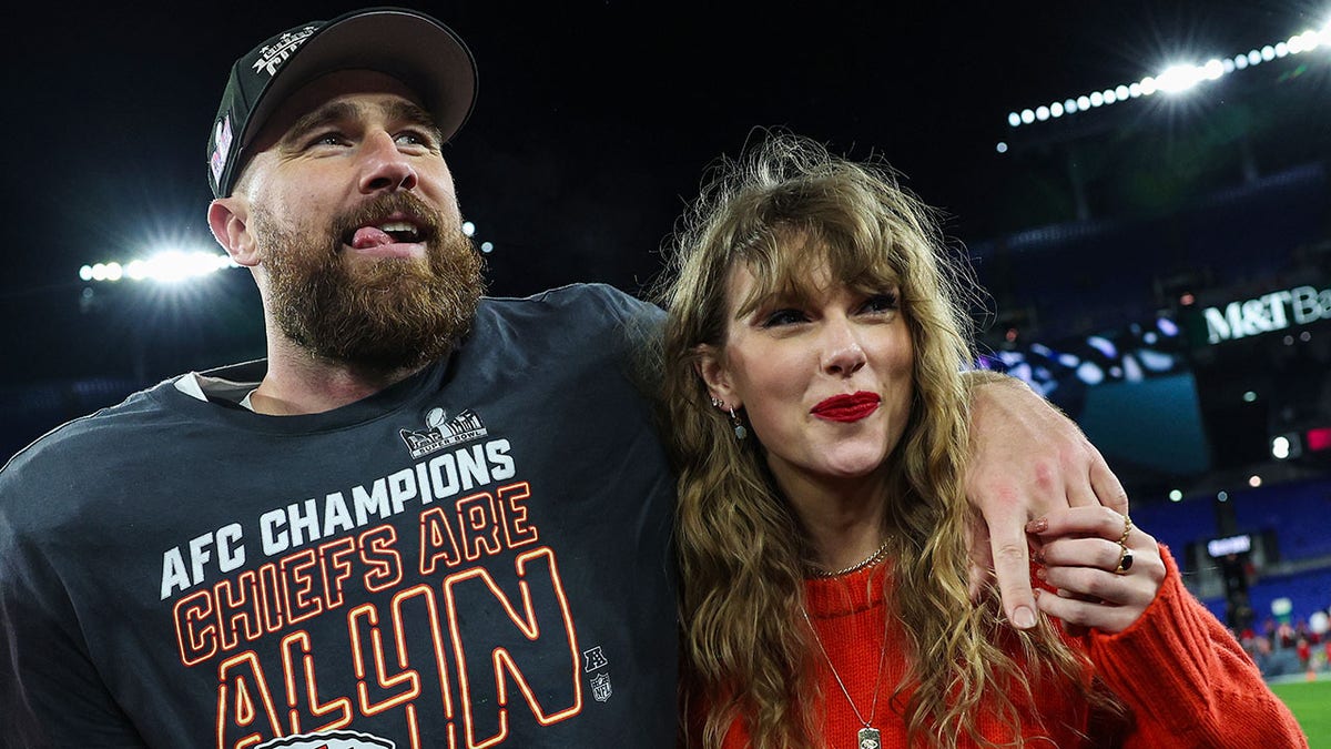 Travis Kelce on the field with his tongue sticking out slightly puts his arm around Taylor Swift after winning the AFC Championship game
