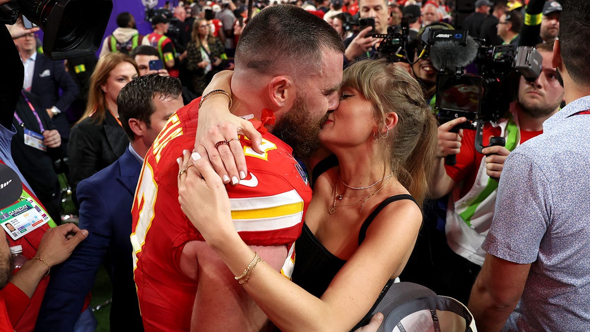 Taylor Swift wraps her arms around Travis Kelce in his red jersey after he wins the Super Bowl on the field