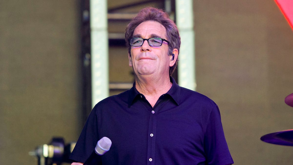 Huey Lewis standing on stage with a microphone