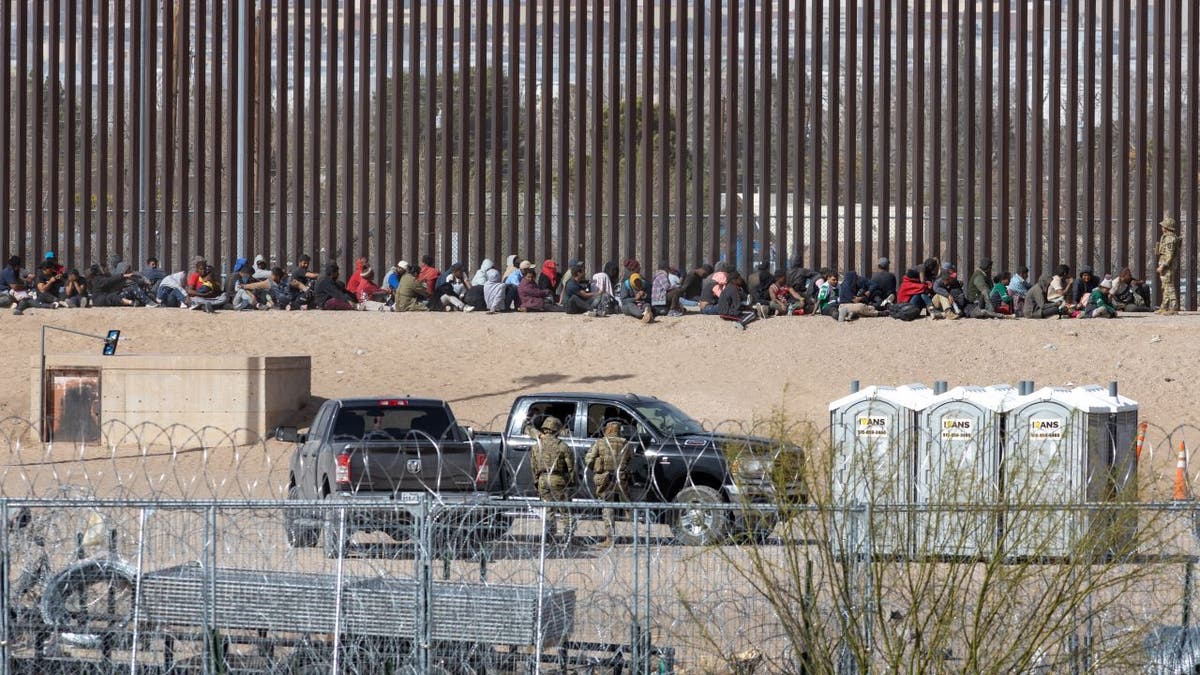 Migrants sitting near border wall
