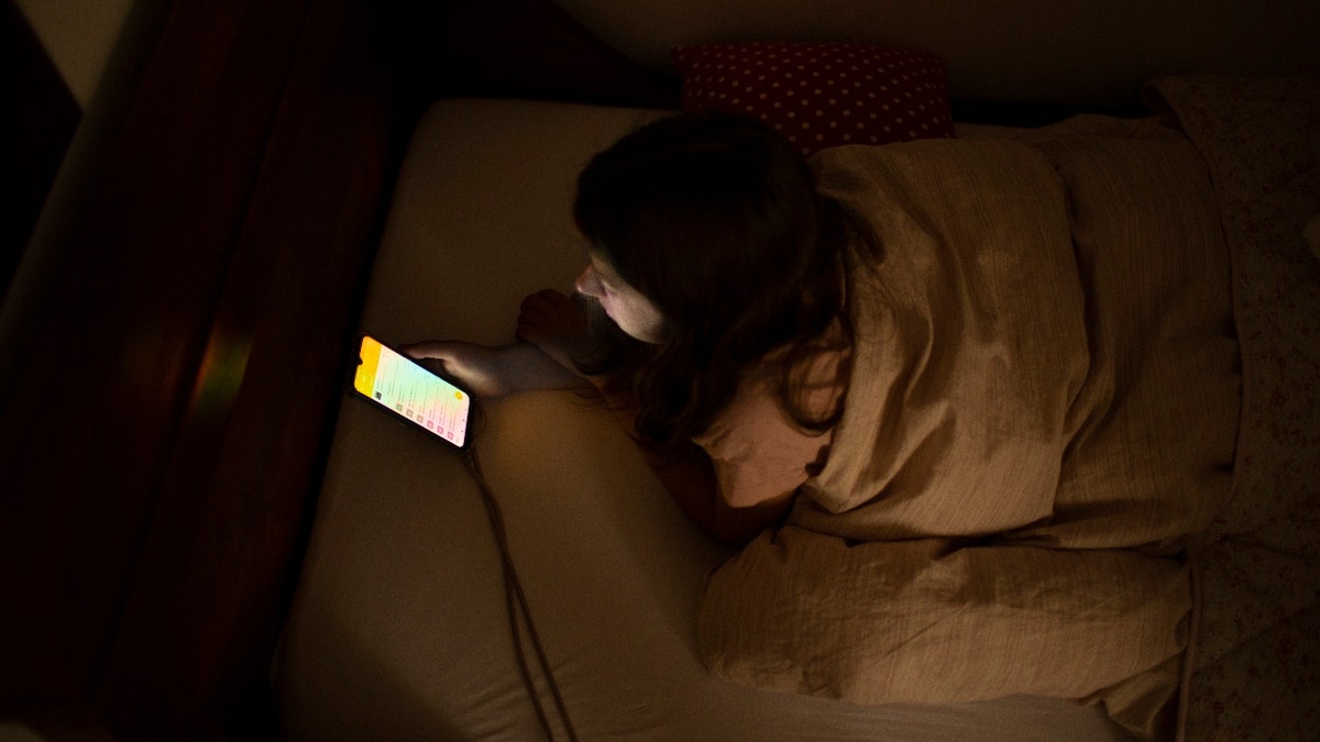 A girl lays on her bed with a phone in her hands